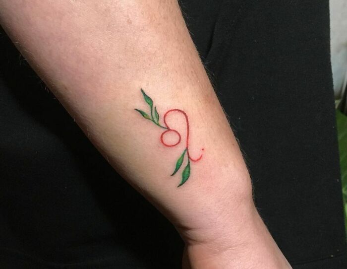 Minimalistic zodiac tattoo of Leo symbol with green leaves on forearm.