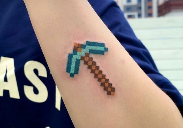Pixelated pickaxe Minecraft tattoo on forearm, ideal for a hardcore gamer.