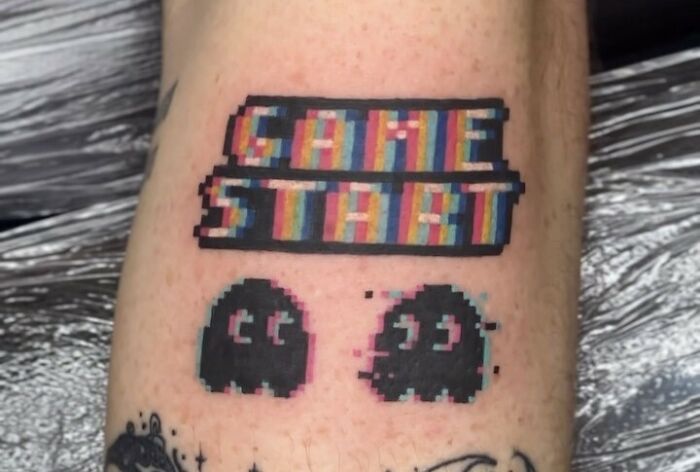 Pixelated "Game Start" tattoo with retro Pac-Man ghosts, perfect for hardcore gamers.