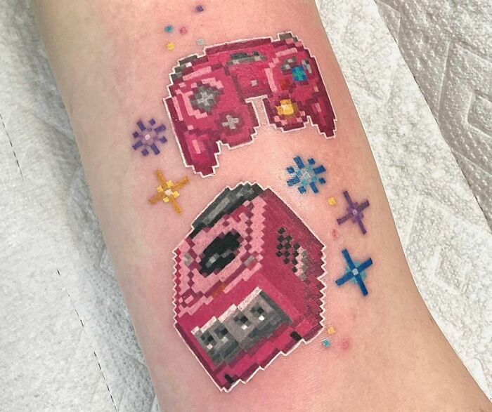 Pixel art video game tattoo with pink console and controller on arm.