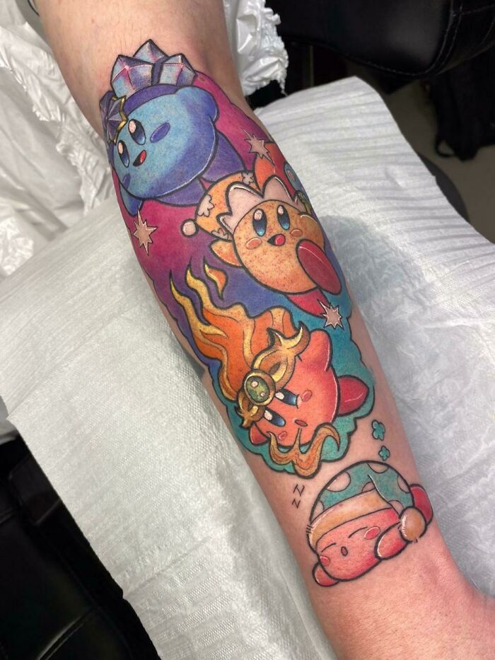 Colorful video game tattoo on forearm featuring multiple Kirby characters in vibrant hues.