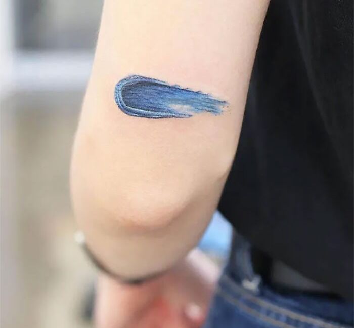 Blue brushstroke elbow tattoo design on a person's arm.