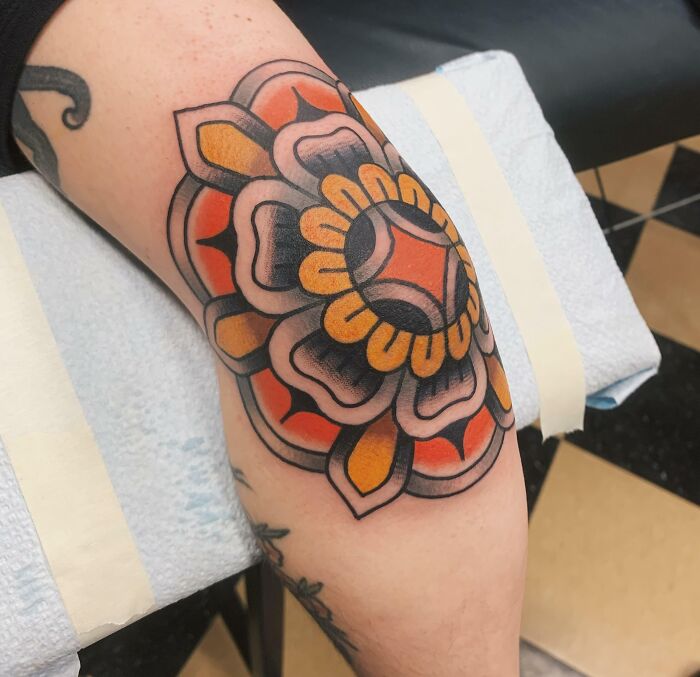 Colorful mandala elbow tattoo with orange and black details on a person's arm.