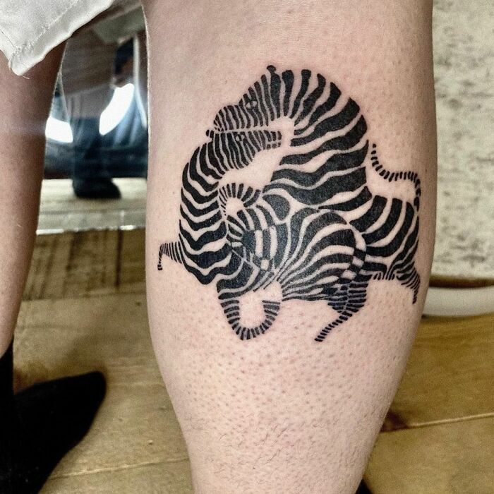 Optical illusion tattoo of intertwined zebras on a leg, creating a mind-bending design.