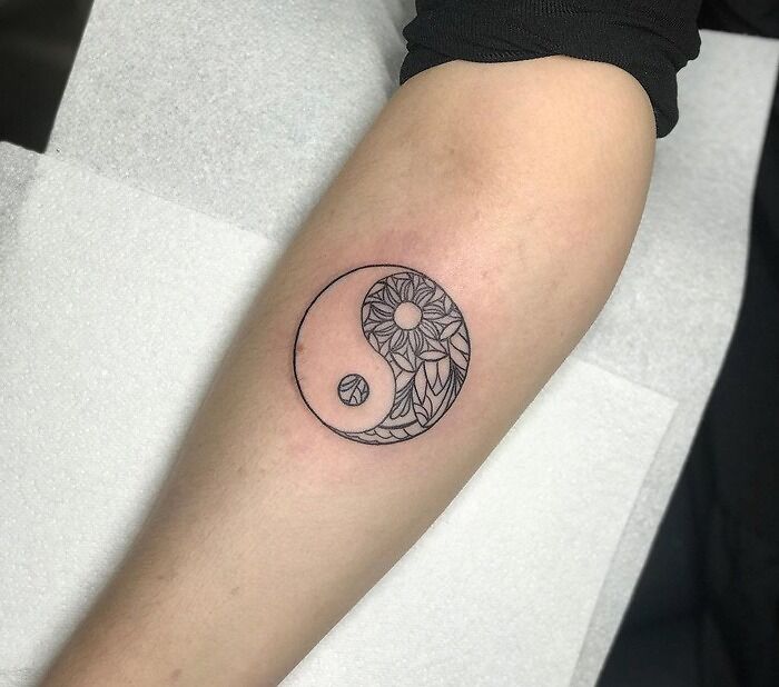 Yin yang tattoo on forearm with floral pattern design, symbolizing duality.