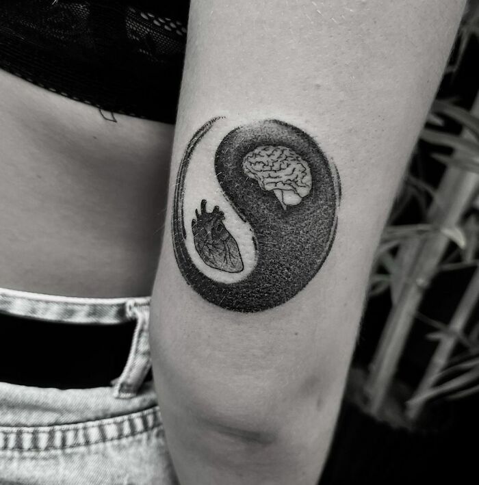 Yin yang tattoo featuring a heart and brain, symbolizing duality on an arm.