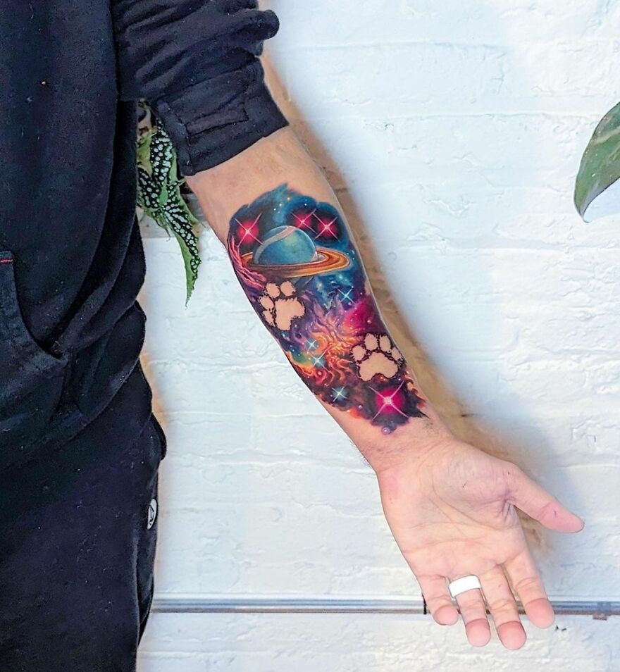 Colorful space tattoo on forearm with Saturn and stars, blending cosmic and artistic elements.