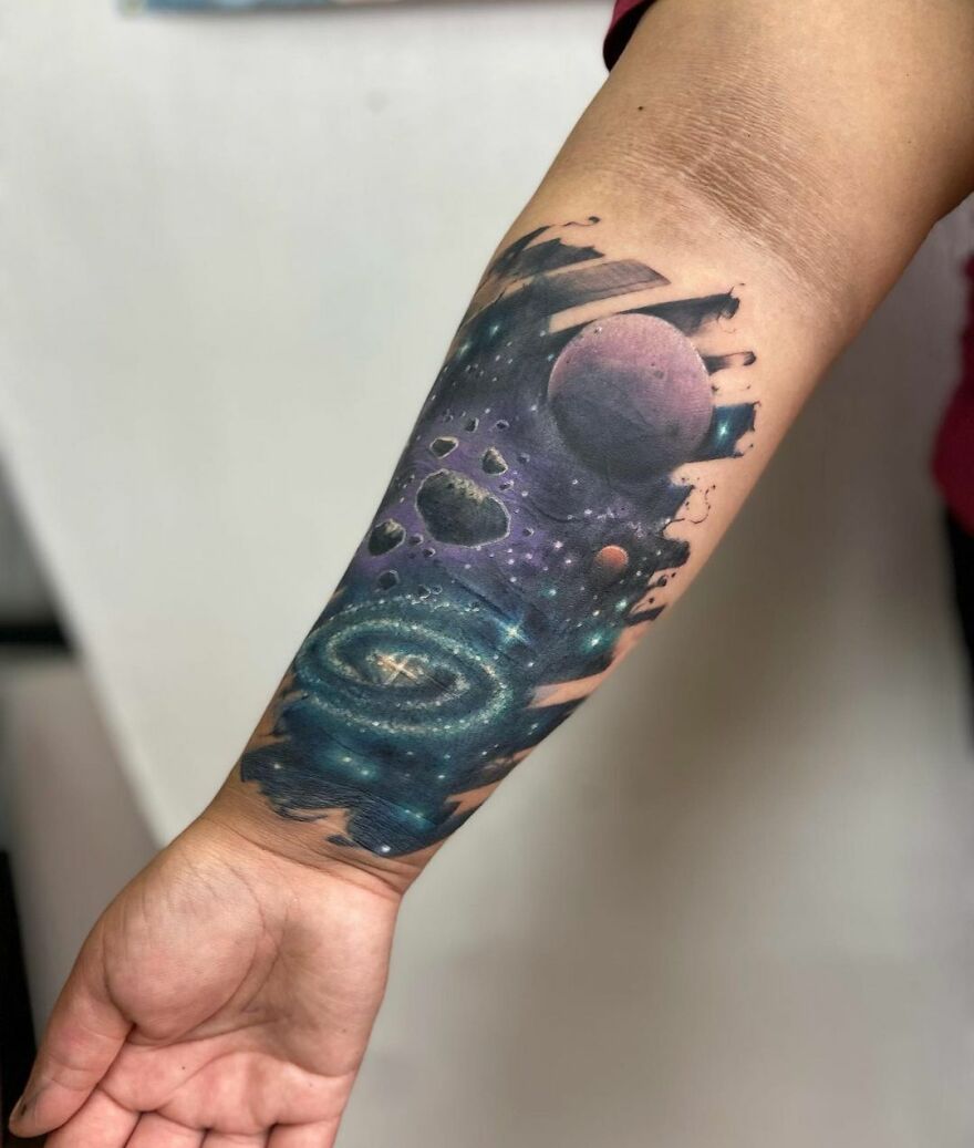 Tattoo of outer space on forearm, featuring galaxy, planets, and stars.