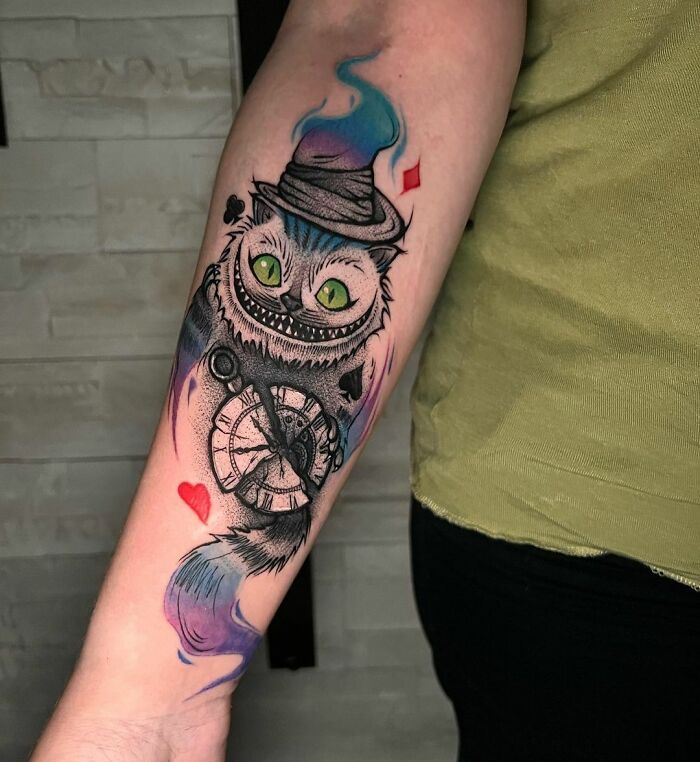 Cartoon tattoo featuring a grinning cat with a clock and hat, inspired by favorite animated shows, on a person's forearm.