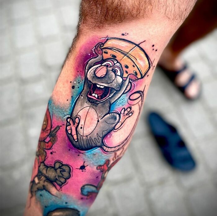 Cartoon tattoo of a joyful Ratatouille mouse holding cheese, inspired by animated shows, on a person's leg.