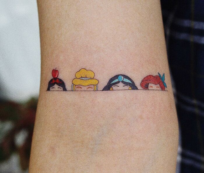 Cartoon tattoo of four princesses' heads peeking above a line, inspired by classic animated shows.