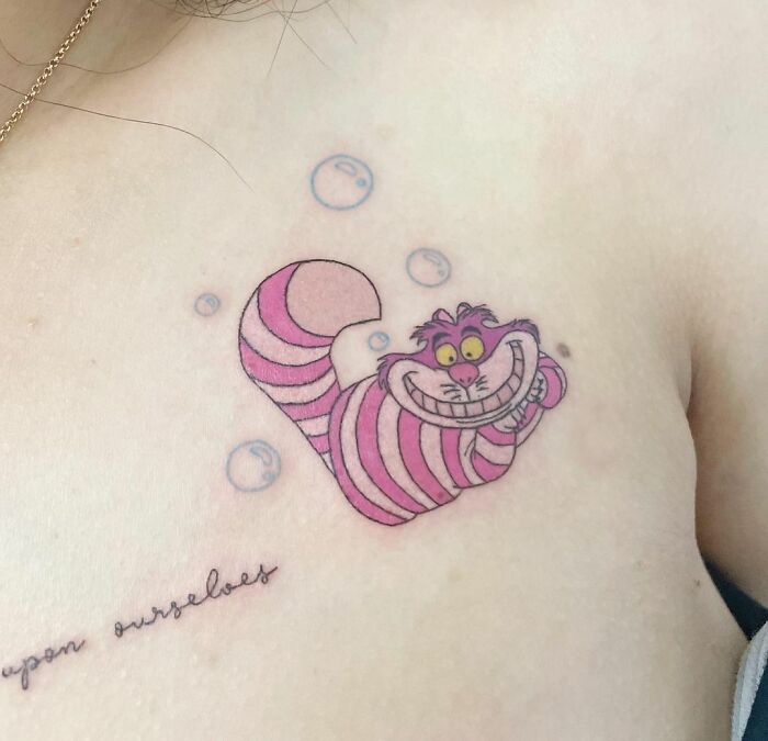 Cartoon tattoo of a grinning pink striped cat, inspired by a favorite animated show, with small bubbles around it.