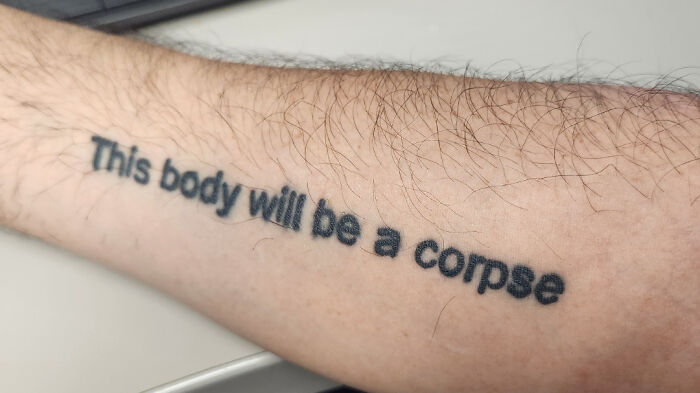 Tattoo reads "This body will be a corpse" on an arm. Reminder to research tattoo artists better.