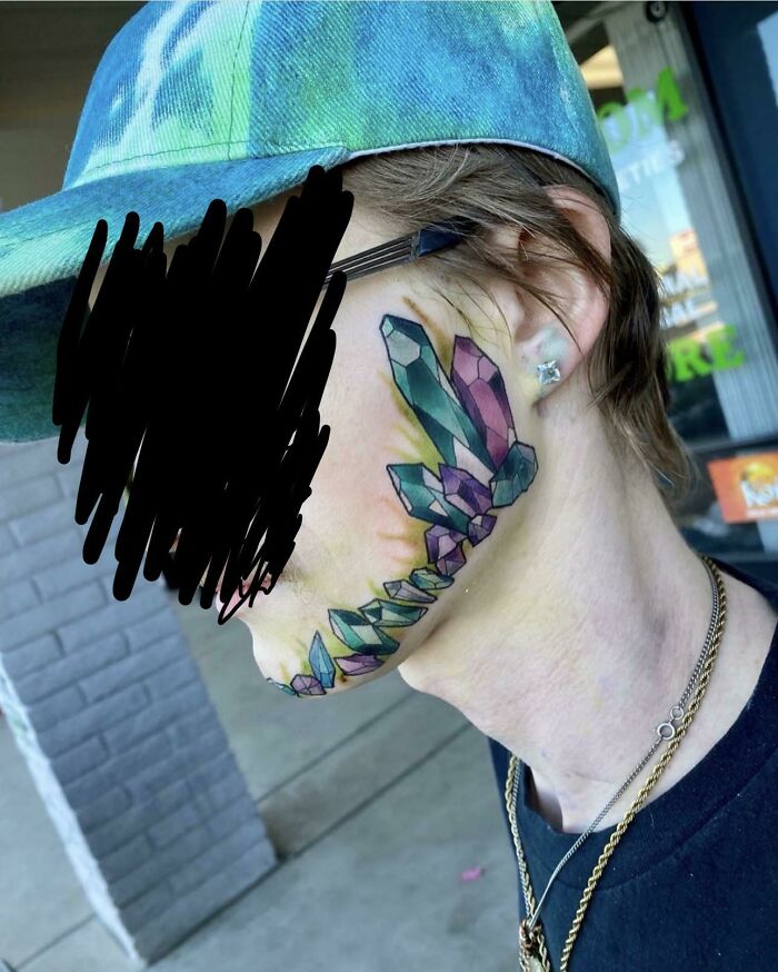 Colorful gemstone tattoo on a person's cheek, possibly by a tattoo artist needing better research.