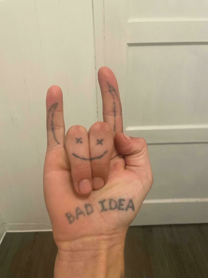 Hand with tattoos showing "BAD IDEA" and smiley face, symbolizing poor tattoo artist research.