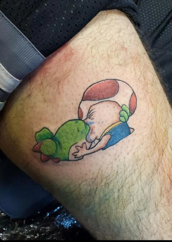 Tattoo of a cartoon character kissing a green creature, showcasing a humorous and unexpected design choice.