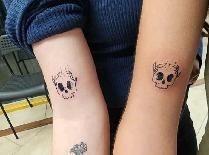 Matching best friend tattoos featuring small, cute skull designs on two arms.