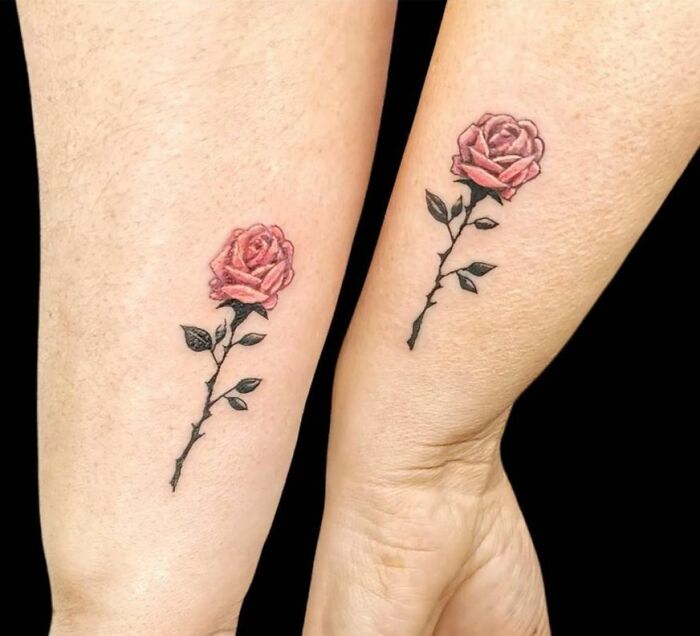 Matching rose tattoos on forearms symbolizing friendship.