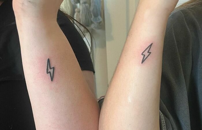 Matching lightning bolt best friend tattoos on forearms, symbolizing friendship.