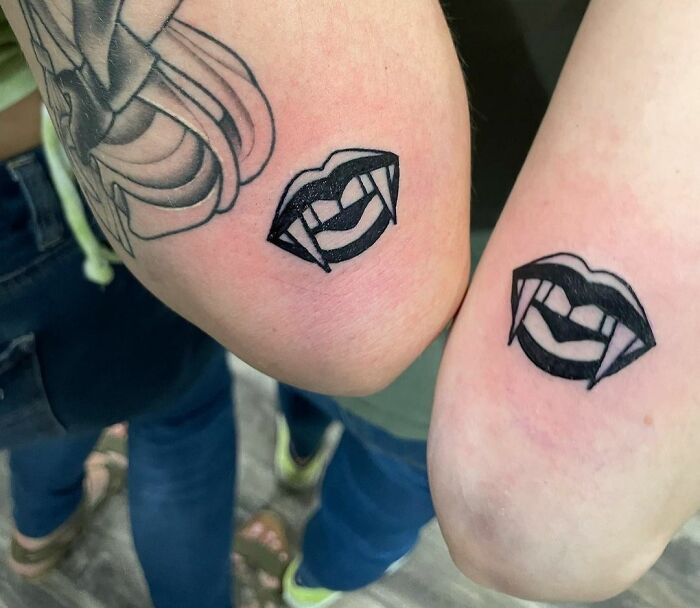 Matching vampire lips tattoos on two elbows, symbolizing friendship.