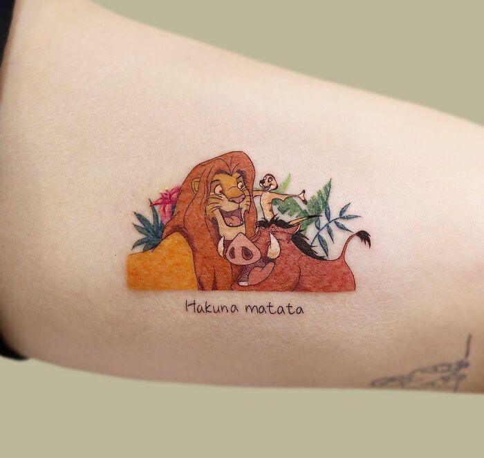 Cartoon tattoo featuring characters Timon, Pumbaa and Simba from a classic animated movie with the phrase "Hakuna Matata" below.