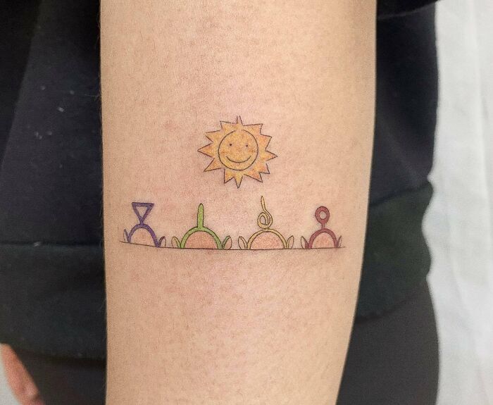 Cartoon tattoos featuring colorful geometric designs with a smiling sun on an arm.
