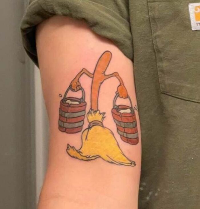 Cartoon tattoo of a broom carrying two water buckets on an arm, evoking nostalgia.