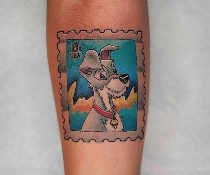 Cartoon tattoo of a classic animated dog character in a postage stamp style on forearm.