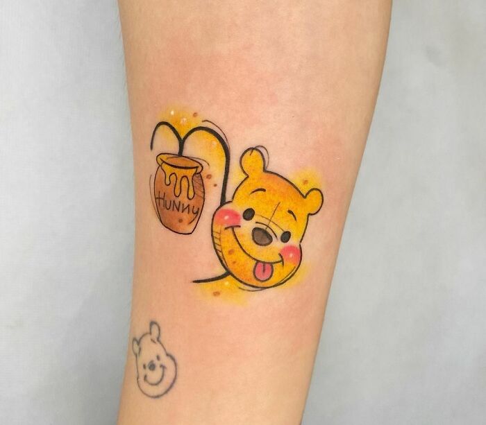 Cartoon tattoo featuring a beloved bear Pooh holding a honey pot on a person's arm.