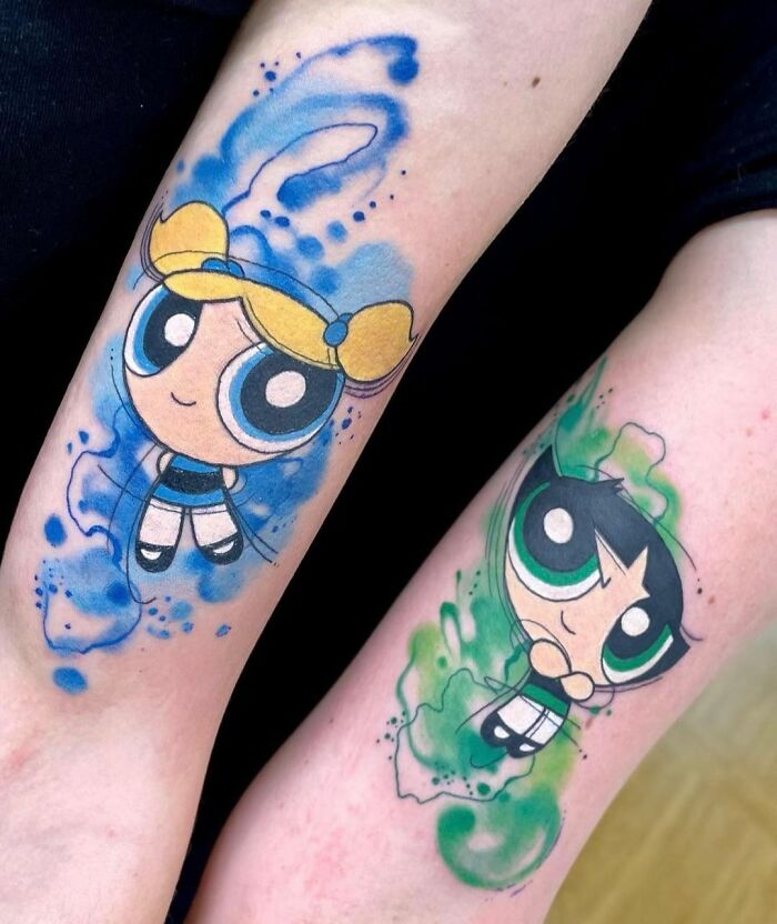 Cartoon tattoos of two characters Bubbles and Buttercup on arms with colorful watercolor effects.