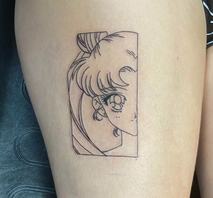 Cartoon tattoo showing half of a Sailor moon character's face on the thigh.