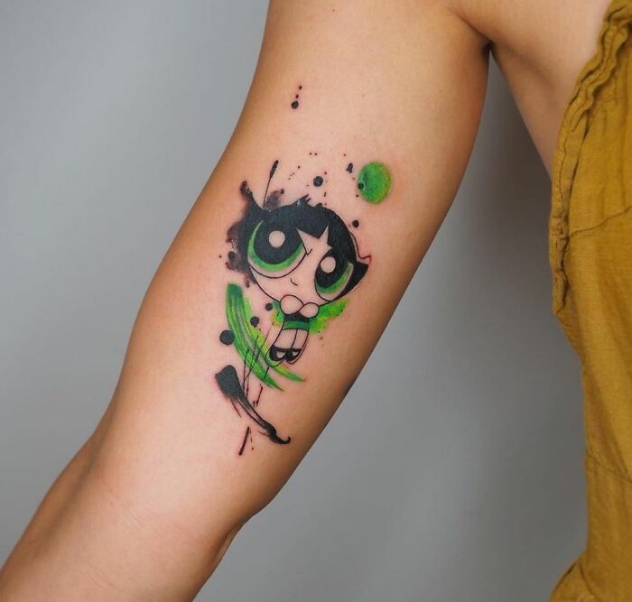 Cartoon tattoo of a green-eyed character Buttercup on arm, featuring vibrant splash art style.