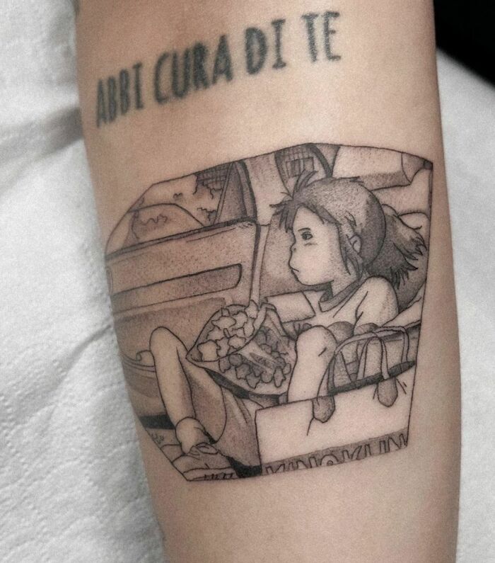 Cartoon tattoo featuring a nostalgic anime character sitting with bags and flowers, surrounded by text.