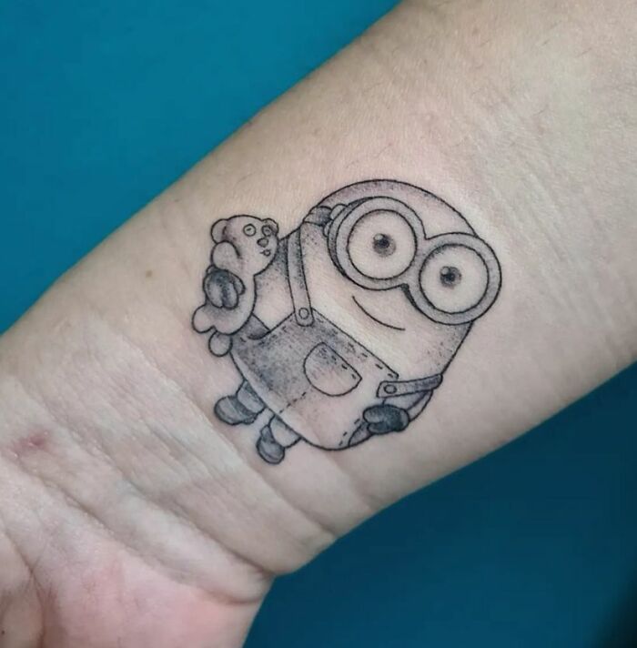 Cartoon tattoo of a small Minion character with goggles and overalls on an arm.