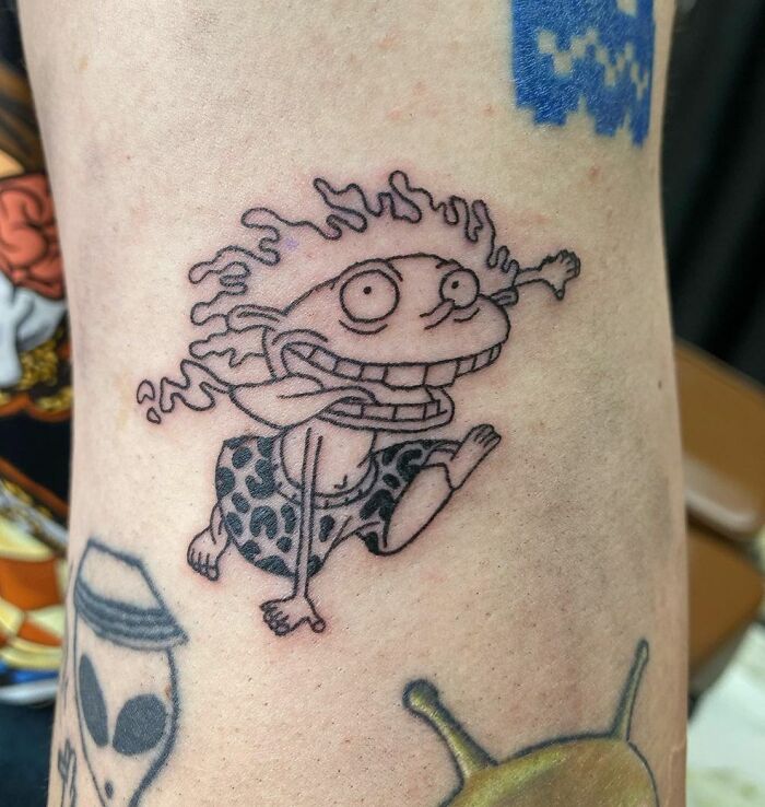 Cartoon tattoo of a wild-haired character Donnie in spotted clothing on an arm, showcasing nostalgic body art.