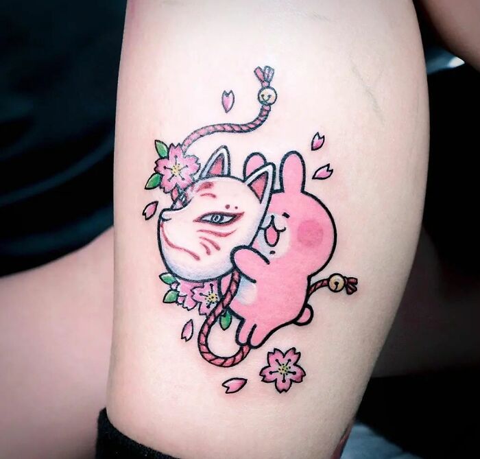 Cartoon tattoo of a pink bunny Kanahei with a fox mask and cherry blossoms on an arm.