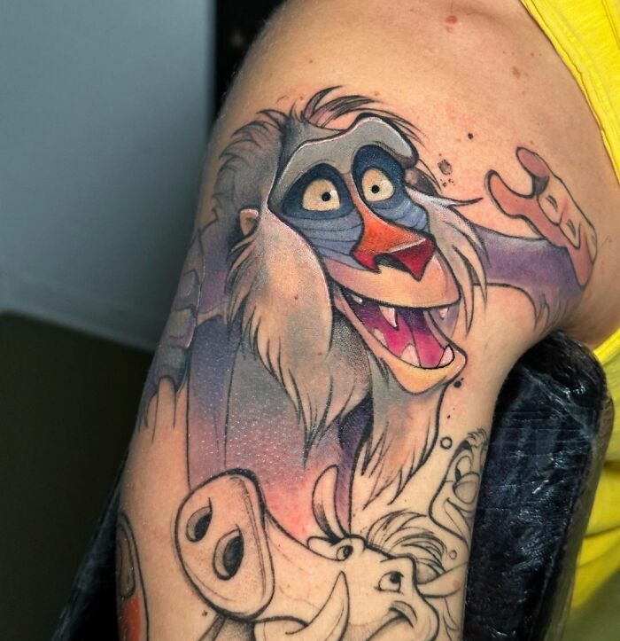 Colorful cartoon tattoo of a vibrant character Rafiki on someone's arm, showcasing classic animation style.