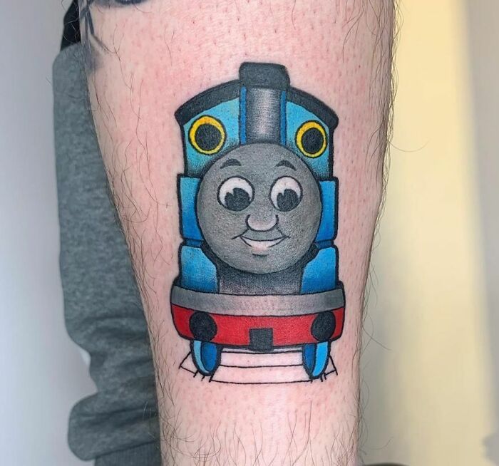 Cartoon tattoo of a cheerful train Thomas The Tank character on a person's leg.