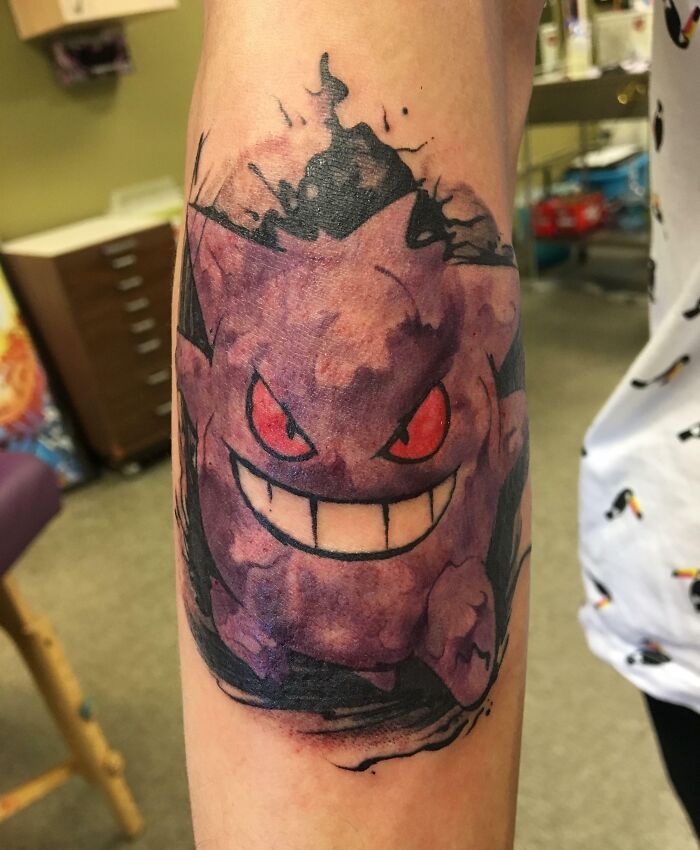 Purple cartoon tattoo of Gengar on forearm with bold colors and intricate design.