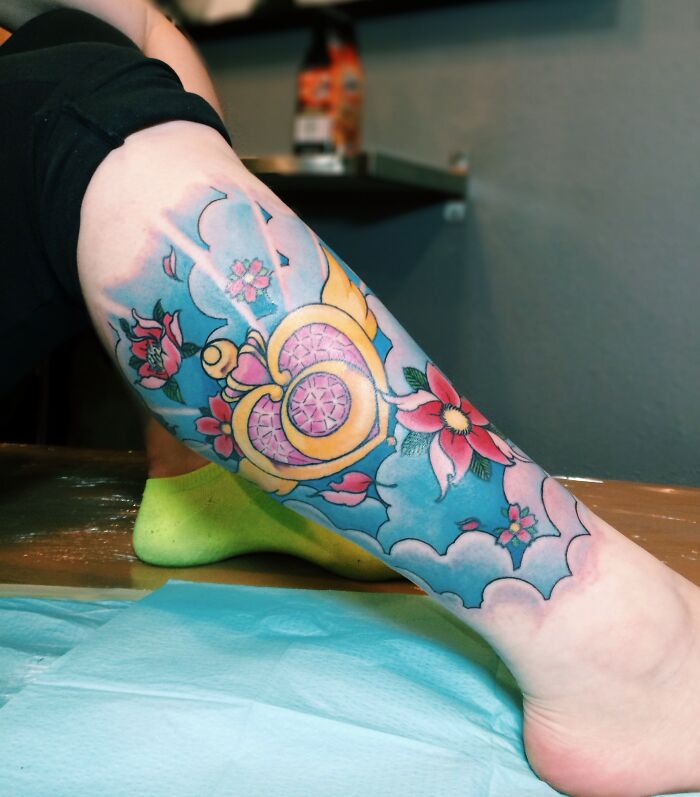 Colorful cartoon tattoo of Sailor Moon on a leg with flowers and a heart-shaped lock, showcasing vibrant retro design.