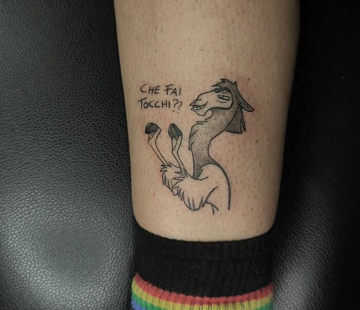 Cartoon tattoo of a llama with text "Che fai tocchi?" on a person's leg, wearing rainbow socks.