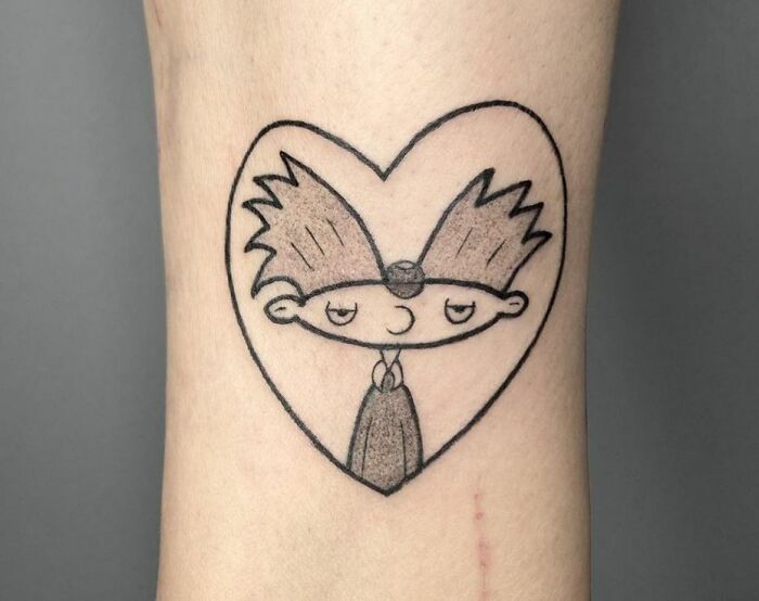 Cartoon tattoo featuring a character with spiky hair inside a heart shape.
