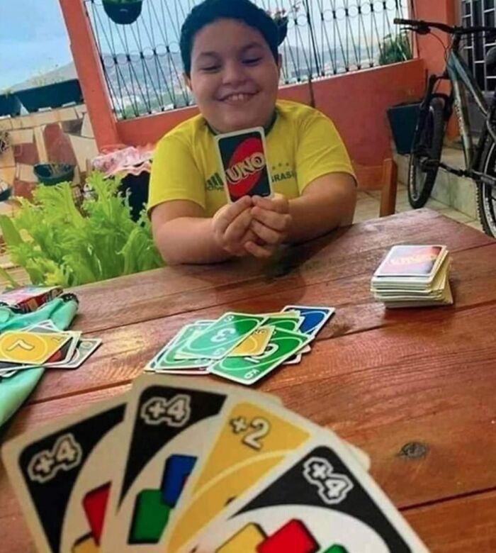 Child holding an Uno card with a mischievous grin, exemplifying a weird meme moment in a casual setting.