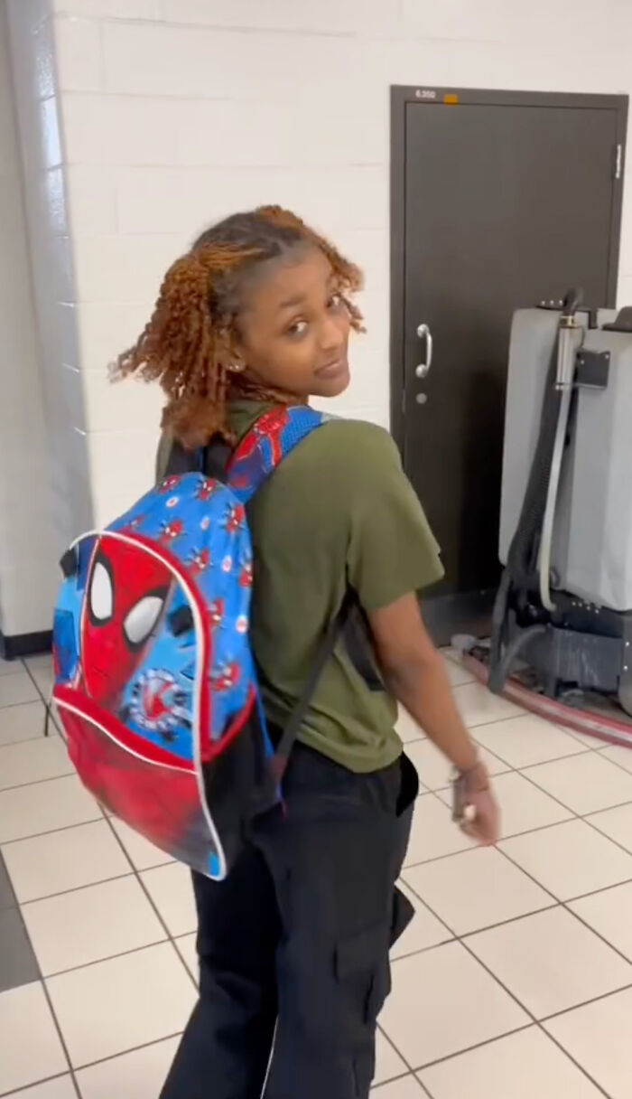 High school senior wearing a colorful kindergarten backpack, looking over their shoulder in a school hallway. High school senior wearing a colorful kindergarten backpack, looking over their shoulder in a school hallway.
