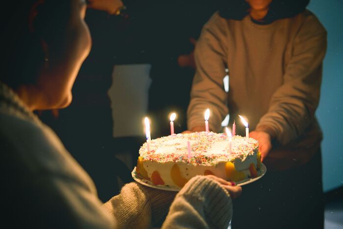 Person holding a birthday cake with lit candles, capturing deep moments shared in an online group setting.