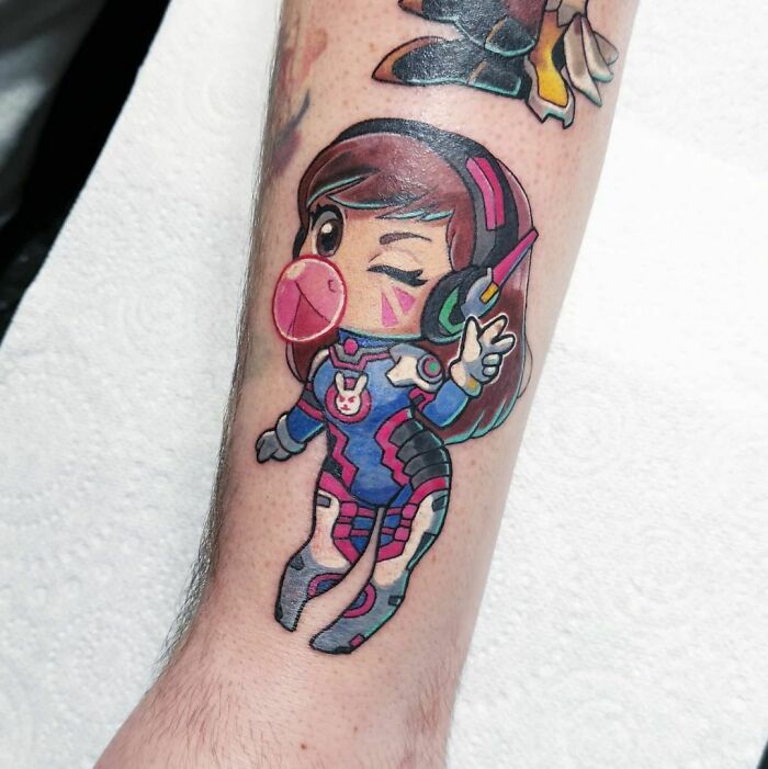 Overwatch video game tattoo of a cute character in blue armor, winking and blowing bubblegum on an arm.