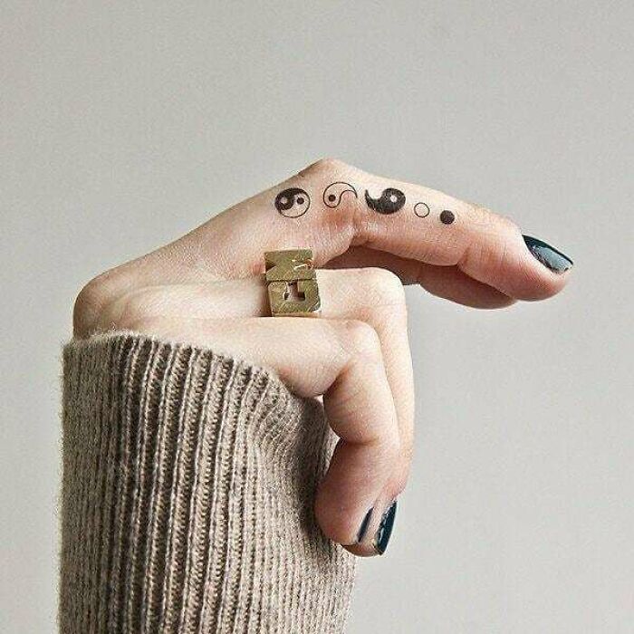 Yin yang tattoos on finger, showcasing duality with minimalist design.