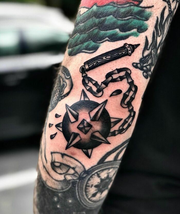 Elbow tattoo featuring a spiked mace with chain, vibrant colors, and intricate design elements.