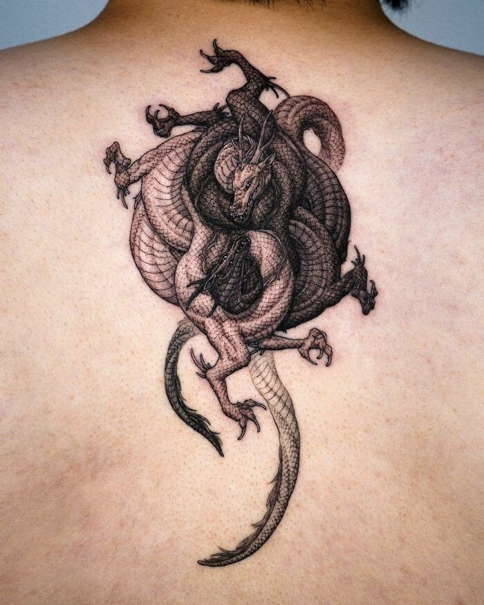 Intricate yin yang tattoo with intertwined dragons, symbolizing balance and duality, on someone's back.