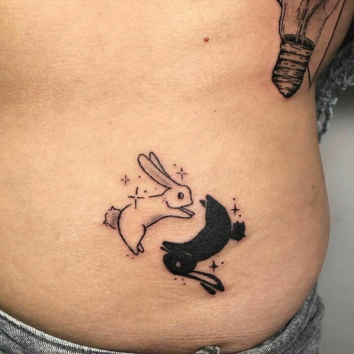 Yin Yang rabbit tattoo illustrating life's duality with black and white bunnies on skin.